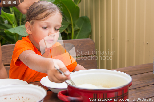 Image of Girl scoop ladle porridge from the pot
