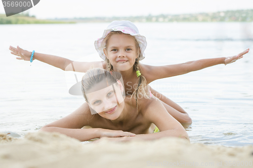 Image of Mom and daughter lying on the sand on the bank of the river