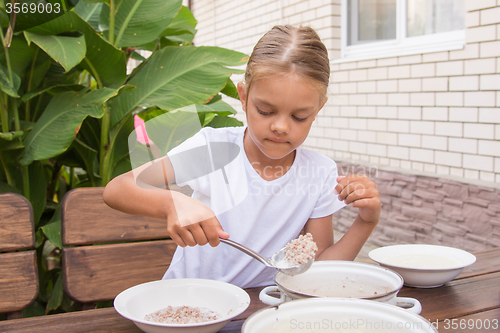 Image of Girl with a ladle of porridge shifts the pan in a bowl