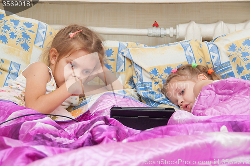 Image of Two girls lying in bed looking at a tablet computer