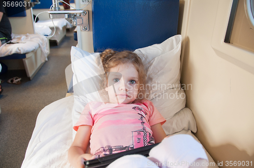 Image of Frightened girl lying on the bed with a tablet in the car with reserved seats