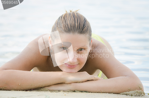 Image of Twenty-five year girl lies on her stomach on the river bank