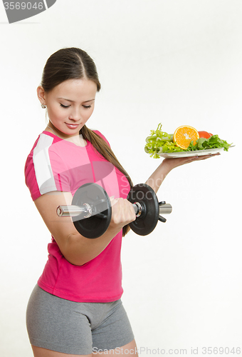 Image of Beautiful athlete with a dumbbell in one hand and a plate of fruit in another