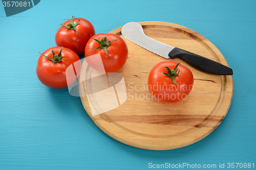 Image of Four tomatoes on a chopping board with a knife