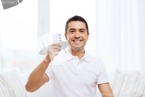 Image of happy man showing pack of pills at home