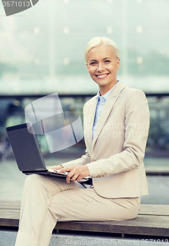 Image of smiling businesswoman working with laptop outdoors