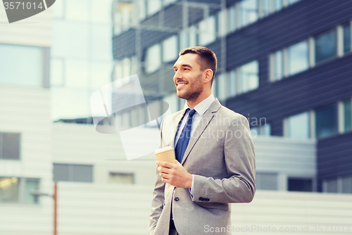 Image of young serious businessman with paper cup outdoors