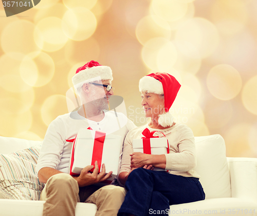 Image of happy senior couple in santa hats with gift boxes