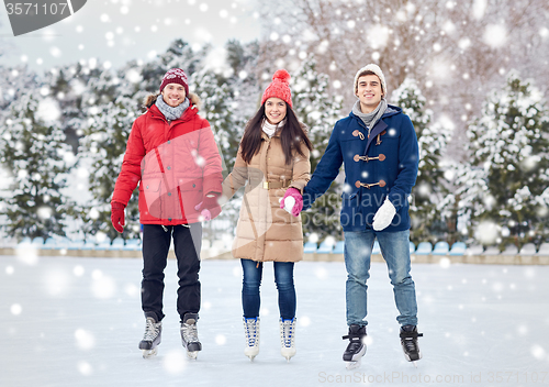 Image of happy friends ice skating on rink outdoors