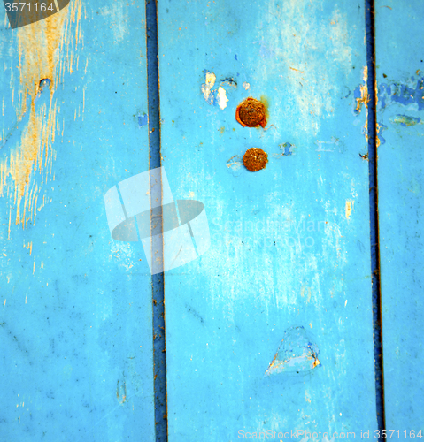 Image of dirty stripped paint in the blue wood door and rusty nail