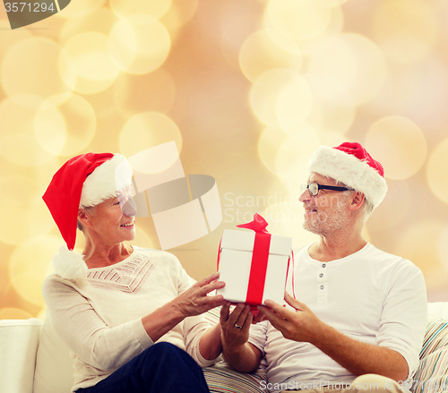 Image of happy senior couple in santa hats with gift box