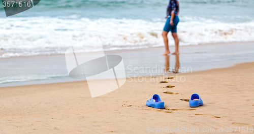 Image of Beach Slippers and Blurred Silhouette of a Woman in Waves 