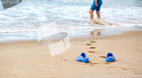 Image of Beach Slippers and Blurred Silhouette of a Woman in Waves 