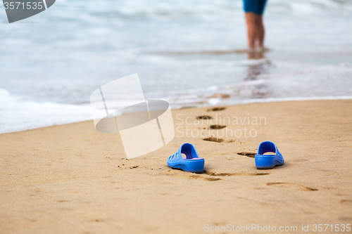 Image of Beach Slippers and Blurred Silhouette of a Woman in Waves 