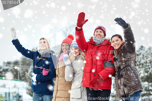 Image of happy friends waving hands on ice rink outdoors