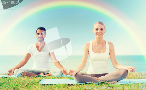 Image of smiling couple making yoga exercises outdoors