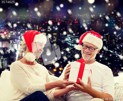 Image of happy senior couple in santa hats with gift box