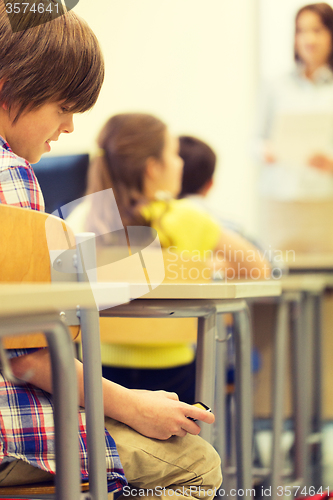 Image of school boy with smartphone on lesson at classroom