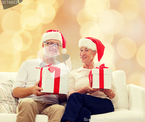 Image of happy senior couple in santa hats with gift boxes