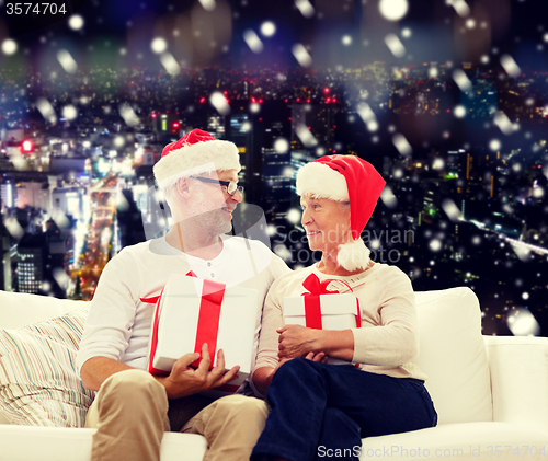 Image of happy senior couple in santa hats with gift boxes