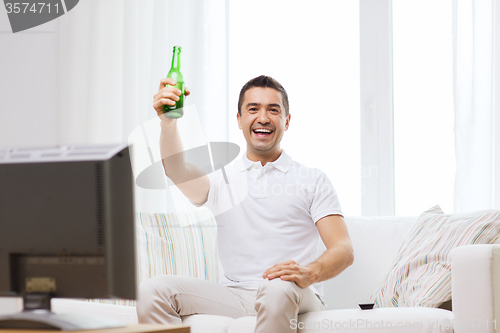 Image of smiling man watching tv and drinking beer at home