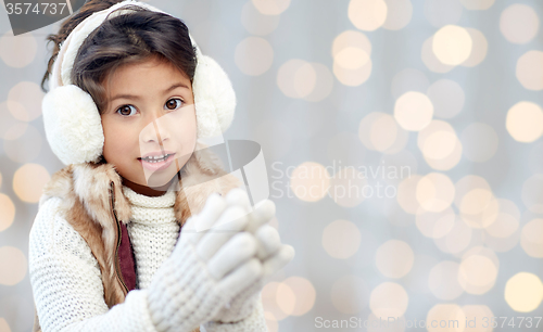 Image of happy little girl in earmuffs over holidays lights