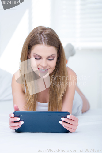 Image of Smiling girl relaxing on her bed with a tablet-pc