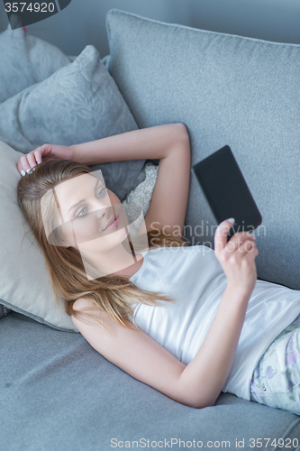Image of Young woman relaxing reading on her tablet