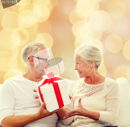 Image of happy senior couple with gift box at home