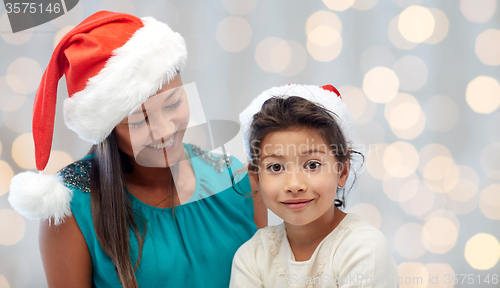 Image of happy mother and little girl in santa hats at home