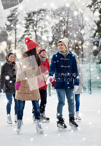 Image of happy friends ice skating on rink outdoors