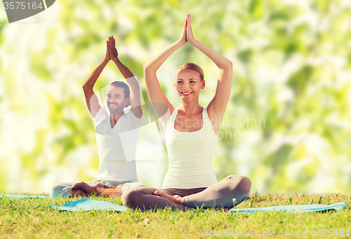 Image of smiling couple making yoga exercises outdoors