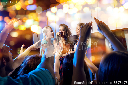 Image of happy young women singing karaoke in night club