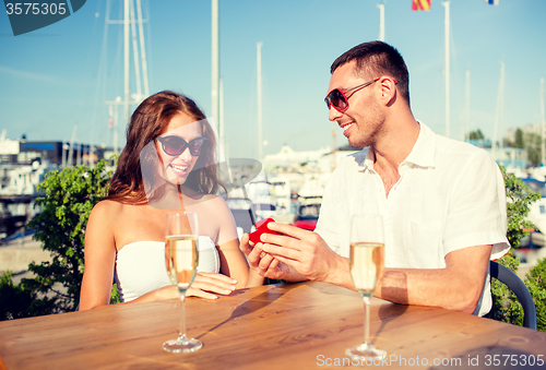 Image of smiling couple with champagne and gift at cafe