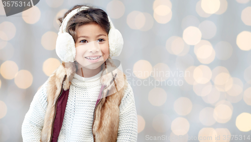 Image of happy little girl in earmuffs over holidays lights