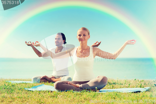 Image of smiling couple making yoga exercises outdoors