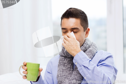 Image of ill man with flu drinking tea and blowing nose