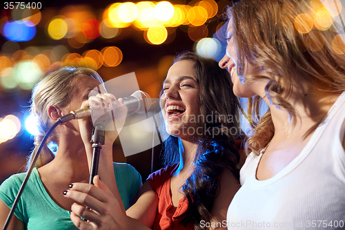 Image of happy young women singing karaoke in night club