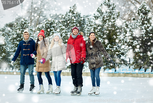 Image of happy friends ice skating on rink outdoors