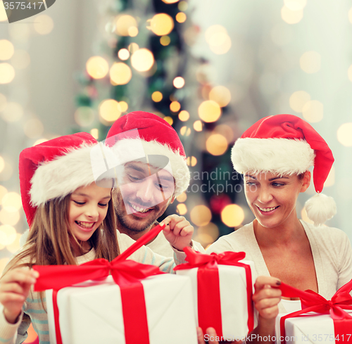 Image of happy family in santa hats sitting with gift boxes