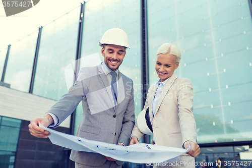 Image of smiling businessmen with blueprint and helmets