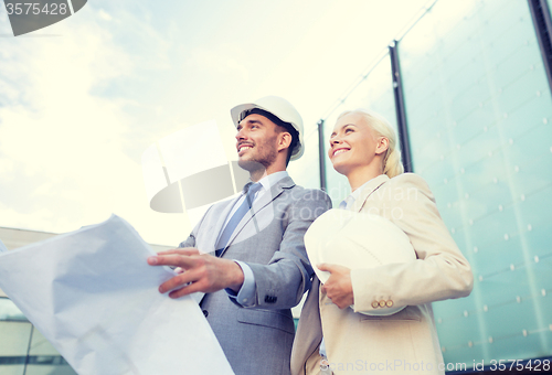 Image of smiling businessmen with blueprint and helmets