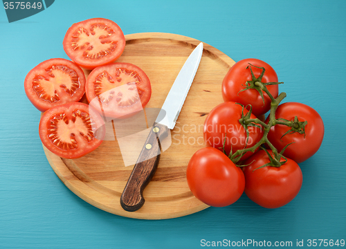 Image of Tomatoes, whole and sliced with knife on wooden board