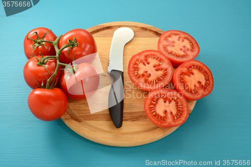 Image of Cutting vine tomatoes with knife on wooden board