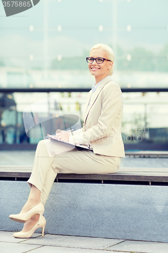 Image of young smiling businesswoman with notepad outdoors