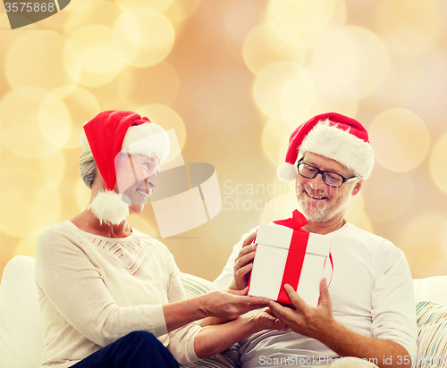 Image of happy senior couple in santa hats with gift box