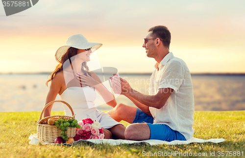 Image of smiling couple with small red gift box on picnic