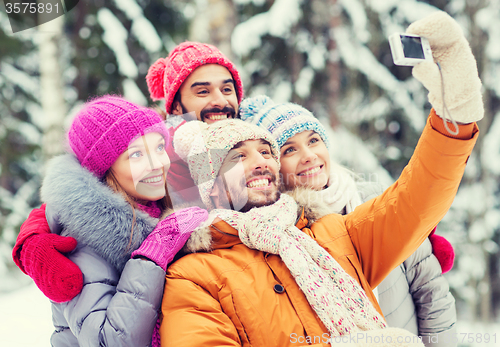 Image of smiling friends with camera in winter forest