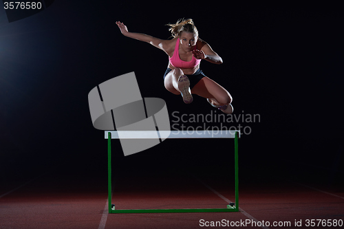 Image of woman athlete jumping over a hurdles