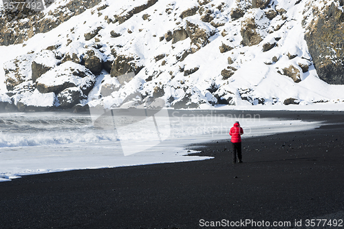 Image of Woman walks along black sand beach in Vik, Iceland